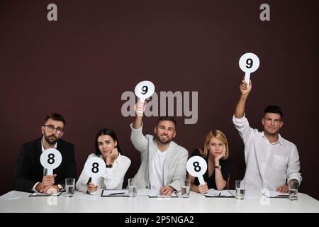 Jury mit unterschiedlichen Punktezeichen am Tisch auf braunem Hintergrund Stockfoto