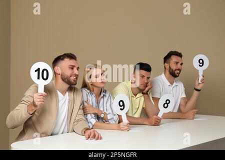 Jury mit unterschiedlichen Punktezeichen am Tisch auf beigefarbenem Hintergrund Stockfoto