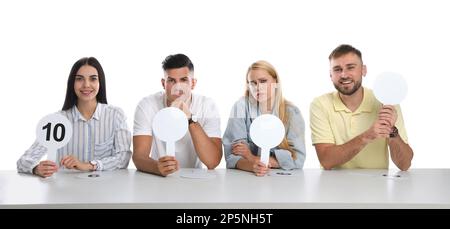 Jury-Gruppe mit unterschiedlichen Emotionen mit leeren Schildern am Tisch auf weißem Hintergrund. Platz für Text Stockfoto