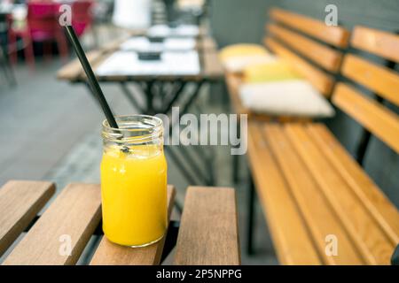 Frisch gepresster Orangensaft in einem Glas mit einem Strohhalm auf einem Holztisch in einem Straßencafé. Stockfoto