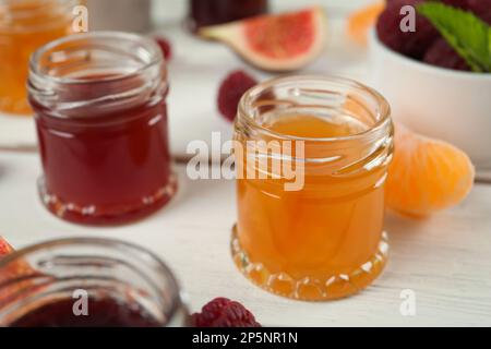 Gläser mit verschiedenen süßen Marmeladen auf weißem Holztisch, Nahaufnahme Stockfoto