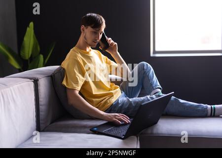 Inhalte junger Mann Entspannen Sie sich auf dem Sofa Verwenden Sie Ihr Smartphone Verbringen Sie Ihre Freizeit online im Chat in sozialen Netzwerken in der Web-App Spielen Sie einfach online. Ein lächelnder Typ hält modern Stockfoto