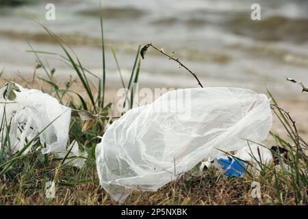 Plastikmüll verstreut auf Gras in der Nähe des Flusses Stockfoto