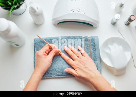 Frau, die Nägel vorbereitet, um Gel-Hybrid-Politur mit UV-Lampe anzuwenden. Beauty Wellness Spa-Behandlungskonzept. Kosmetikprodukte, UV-Lampe, grüne Blätter auf Whi Stockfoto