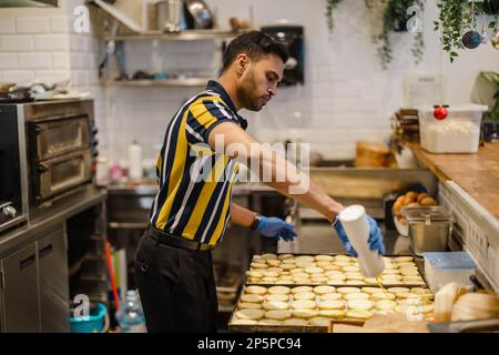 Junger Mann, der in der kommerziellen Küche frisches Essen zubereitet Stockfoto