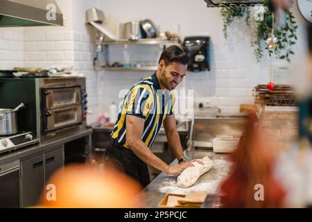 Junger Mann, der in der kommerziellen Küche frisches Essen zubereitet Stockfoto