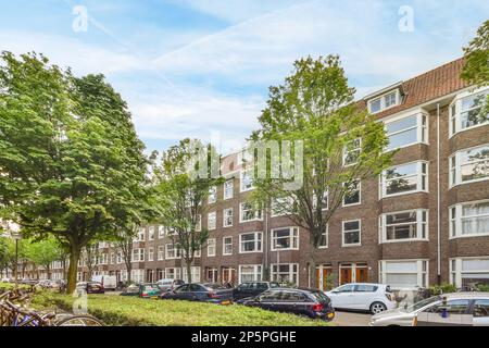 Amsterdam, Niederlande - 10. April 2021: Stadtstraße mit geparkten Autos und Fahrrädern auf dem Gehweg vor Wohngebäuden, stockfoto amsterdam, niederlande Stockfoto