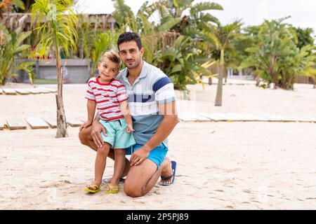 Porträt von glücklichen, birassischen Vater und Sohn, die sich am Strand umarmen und lächeln, in Zeitlupe Stockfoto