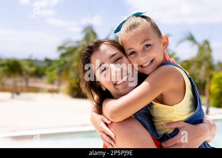 Porträt einer glücklichen, birassischen Mutter und Tochter, die sich am Swimmingpool umarmen Stockfoto