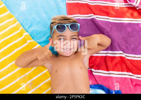 Porträt eines glücklichen, birassischen Jungen, der lächelt und auf einem Handtuch am Swimmingpool liegt Stockfoto