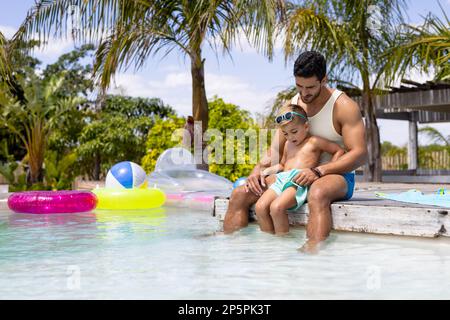 Fröhlicher, birassischer Vater und Sohn, die zusammen im Schwimmbad spielen Stockfoto
