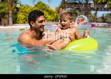 Fröhlicher, birassischer Vater und Sohn, die zusammen im Schwimmbad spielen Stockfoto