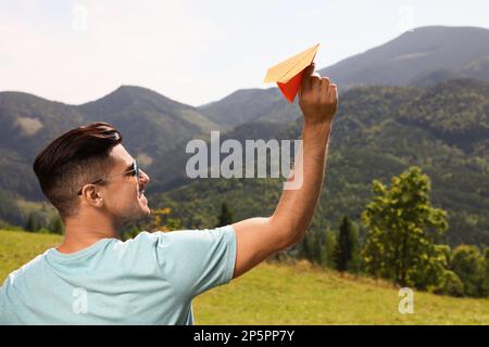 Ein Mann, der ein Papierflugzeug in die Berge wirft, an einem sonnigen Tag Stockfoto