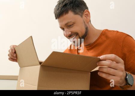 Glücklicher Mann, der das Paket drinnen öffnet. Internet-Shopping Stockfoto