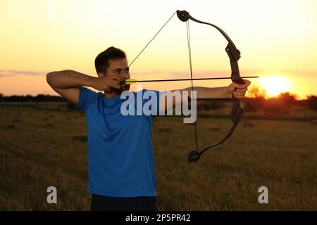 Ein Mann mit Pfeil und Bogen, der bei Sonnenuntergang im Feld Bogenschießen praktiziert Stockfoto