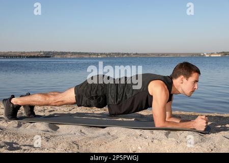 Sportlicher Mann, der Plank-Training am Strand macht Stockfoto