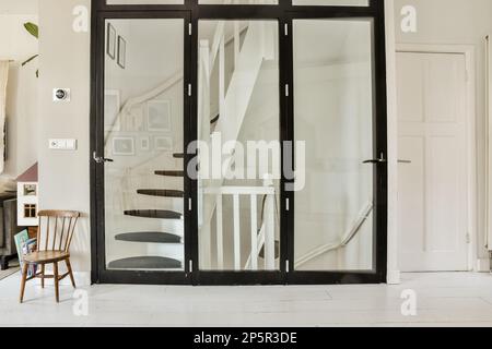 Amsterdam, Niederlande - 10. April 2021: Ein Wohnzimmer mit weißen Wänden und schwarzen Glastüren, die auf die Treppe zum Essbereich führen Stockfoto