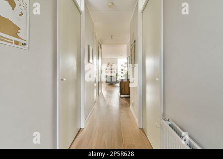 Ein langer schmaler Flur mit weißen Wänden und Holzfußboden auf jeder Seite, der zum Wohnzimmer führt Stockfoto