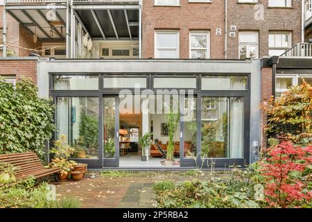 Ein Haus mit vielen Pflanzen und Blumen im Vorgarten, umgeben von hohen Ziegelgebäuden auf beiden Seiten Stockfoto