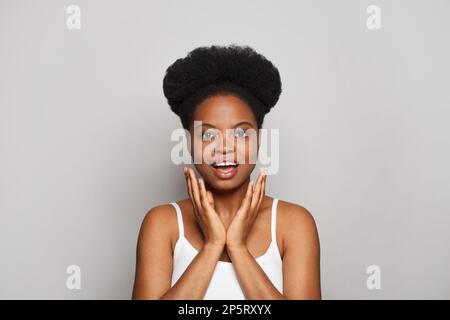 Fröhliche, aufgeregte, fröhliche, überraschte braune Modelin, die vor dem Hintergrund eines weißen Studiobanners in die Kamera schaut Stockfoto