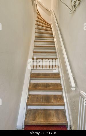 Einige Holztreppen in einer weißen Wand und roter Teppich auf dem Boden, mit einer offenen Tür, die zu einem anderen Zimmer führt Stockfoto