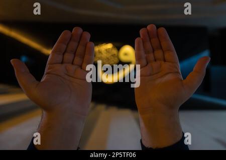 Ramadan oder islamisches Konzeptfoto. Muslimische Gebete mit erhobenen Händen und Kalligraphie im Hintergrund. Selektiver Fokus. Istanbul Turkiye - 11.12.2022 Stockfoto