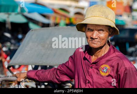 Ein älterer Radfahrer steht neben seinem Fahrradfahrer, während er vor dem Central Market in Phnom Penh, Kambodscha, auf Passagiere wartet. Stockfoto