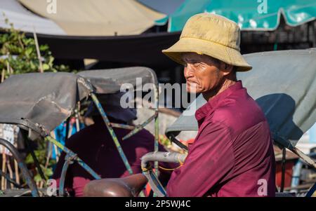 Ein älterer Radfahrer steht neben seinem Fahrradfahrer, während er vor dem Central Market in Phnom Penh, Kambodscha, auf Passagiere wartet. Stockfoto