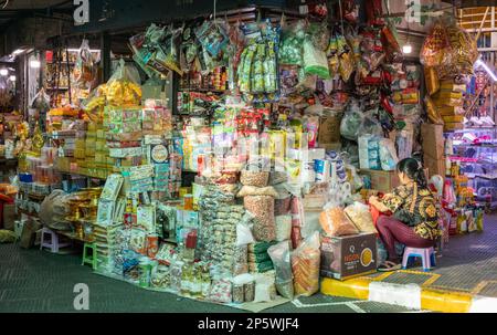 Eine Frau sitzt an ihrem Stand und verkauft Lebensmittel und Haushaltsartikel auf dem Central Market in Phnom Penh, Kambodscha. Stockfoto