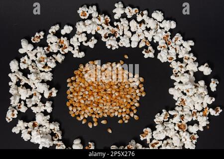 Ein Haufen Maiskörner in der Mitte eines vorgefertigten Popcornkreises, Popcorn auf schwarzem Hintergrund, Nahaufnahme und Kopierbereich. Stockfoto