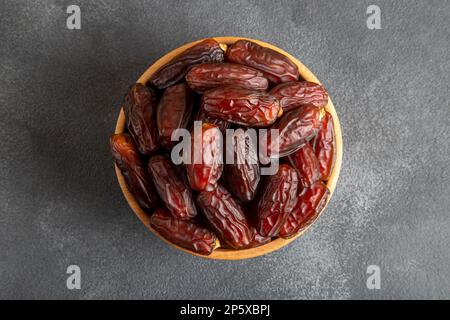 Dattelfrüchte in Holzschüssel auf schwarzem Hintergrund Stockfoto