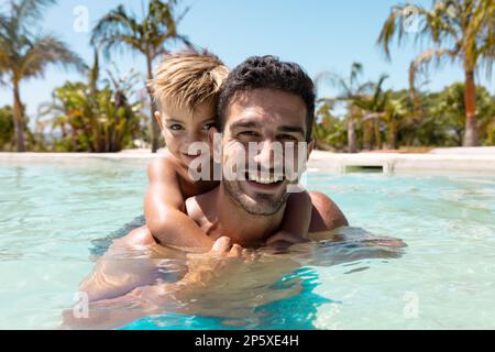 Porträt eines glücklichen, birassischen Vaters und Sohnes, die zusammen im Schwimmbad spielen Stockfoto