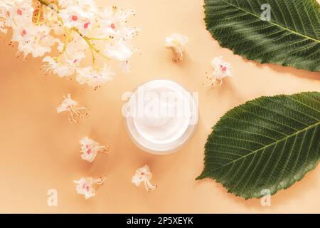 Cremefarbenes Glas und Kastanienblätter und Blumen. Naturkosmetik-Konzept. Draufsicht, flach liegend. Stockfoto