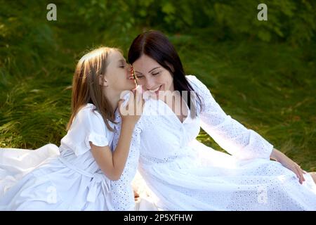 Tochter umarmt ihre Mutter und erzählt ihr alle Geheimnisse beim Picknick in der Natur Stockfoto