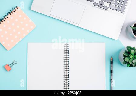 Leerer Notizblock, Laptop, Bleistift und saftige Pflanze auf blauem Hintergrund. Gemütliches Arbeitsplatzkonzept, Arbeit von zu Hause aus. Draufsicht, flaches Lay, Modell. Stockfoto