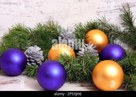 Weihnachtsdekoration mit violetten und goldenen Kugeln, Fichtenzweigen und Pinienzapfen Stockfoto