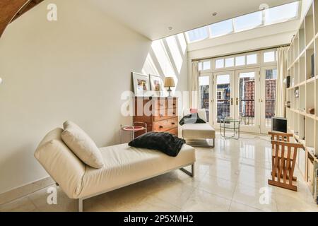 Amsterdam, Niederlande - 10. April 2021: Ein Wohnzimmer mit weißer Couch und Holztisch in der Mitte des Raums ist eine offene Tür, die zu einem Balkon führt Stockfoto