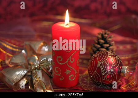 Roter Weihnachtsball mit Kiefernzapfen, goldenes Band und brennende Kerze, Weihnachtsdekoration Stockfoto