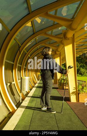 Golfer steht und hält ihren Golfklubfahrer in einem Gebäude auf einer Driving Range auf dem Golfplatz an einem sonnigen Tag in Ascona, Schweiz. Stockfoto