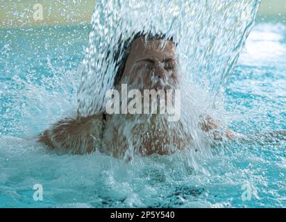 Frauengesicht Entspannen in einem Hydromassage-Pool mit fallendem Wasser in der Schweiz. Stockfoto