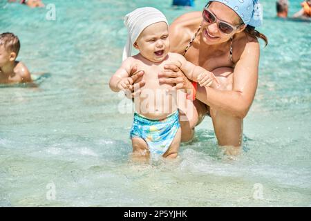 Die Mutter hält den Jungen im Urlaub im Swimmingpool mit klarem blauem Wasser im Wasserpark Stockfoto