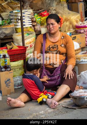 Eine Lebensmittelhändlerin auf einem Straßenmarkt in Phnom Penh, Kambodscha, sitzt neben ihrem Sohn und sieht traurig aus. Stockfoto