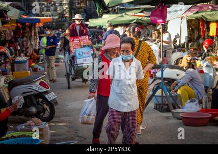 Einkäufer stöbern durch einen Straßenmarkt in Phnom Penh, während ein Radfahrer durch Kisten mit Bier und Getränken fährt. Stockfoto