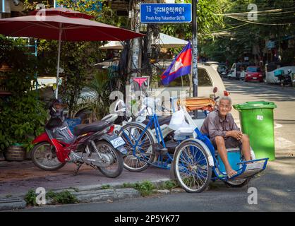 Ein älterer Cyclo-Fahrer wartet mit seinem Fahrradtaxi auf einen Passagier an einer Straßenecke in Phnom Penh, Kambodscha. Stockfoto