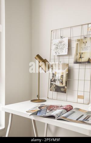 Eine Zeitschrift auf einem weißen Tisch mit einer Lampe und einem Stuhl in der Ecke daneben ist ein Foto des Gesichts einer Frau Stockfoto