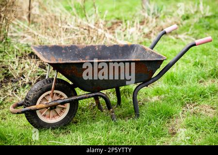 Alter rostiger Gartenwagen auf grünem Gras. Frühjahrsgartenarbeit. Stockfoto