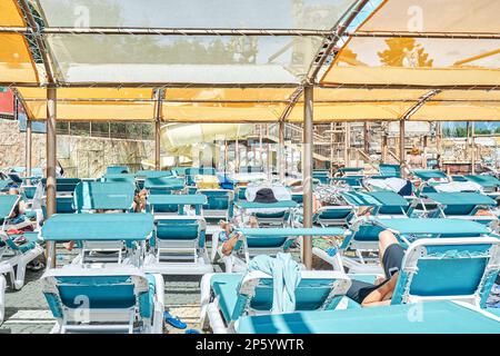 Blaue Sonnenliegen in Reihen unter transparentem Baldachin. Sonnenschutz über den Liegestühlen in der Nähe des Swimmingpools im touristischen Wasserpark Stockfoto