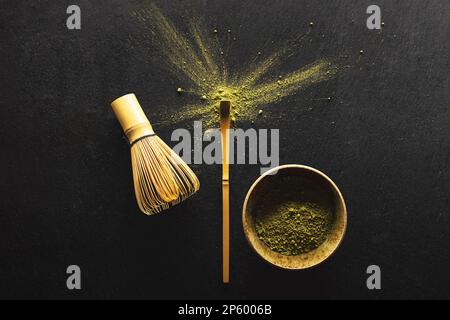 Matcha, Grüntee-Pulver in der Schüssel und Bambusquirl auf schwarzem Hintergrund. Draufsicht. Stockfoto