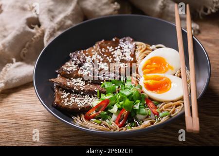 Ramen-Suppe mit Rind, Ei und Schnittlauch auf einem Holztisch Stockfoto