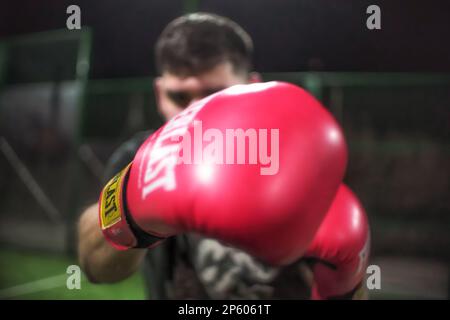 Boxer wirft Jabs und schlägt mit Boxhandschuhen in Zeitlupe mit geringer Schärfentiefe vor die Kamera. Stockfoto